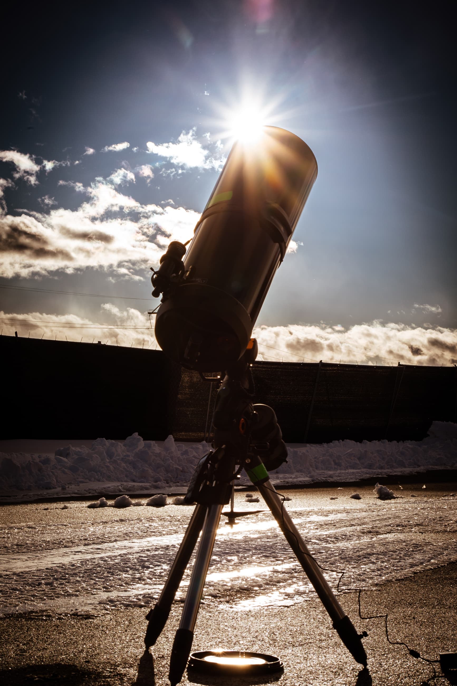 A telescope silhouetted against the sun on a snowy day