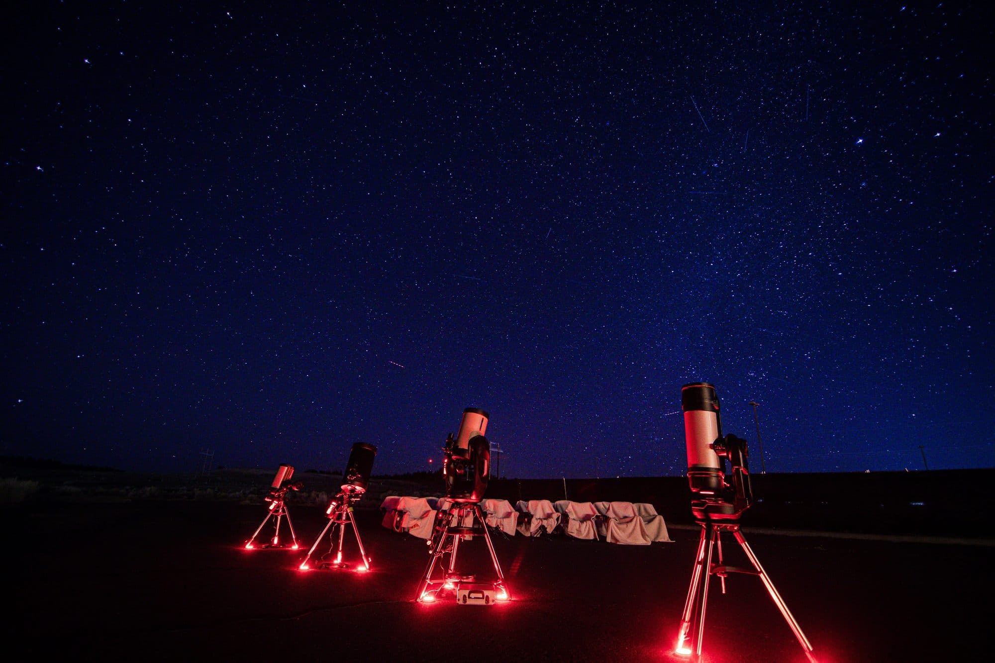 Four telescopes on red footlights beneath a full field of stars