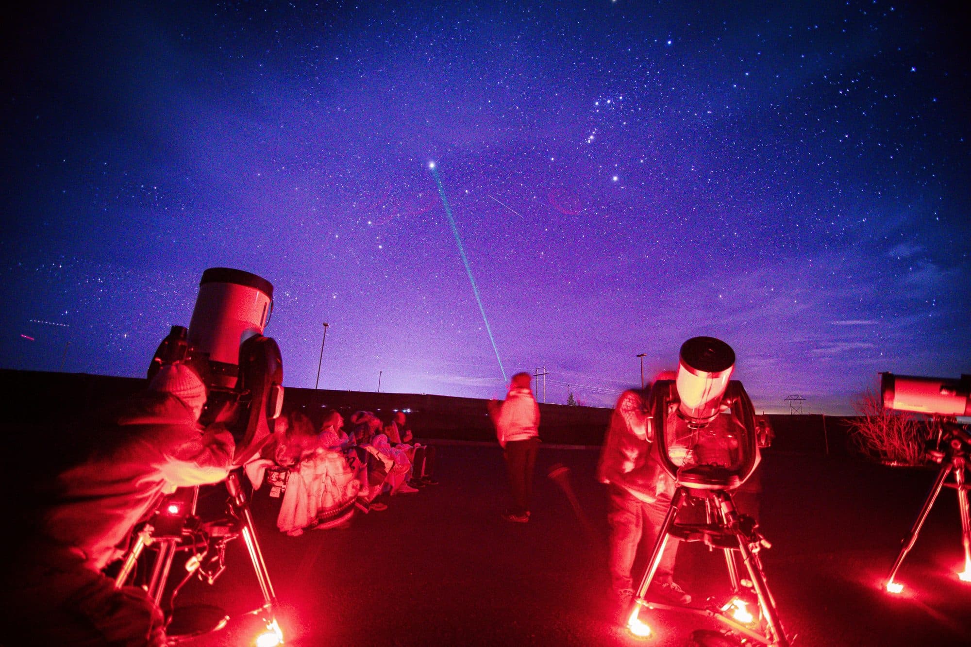 A guide's green laser tracing a constellation above a seated group