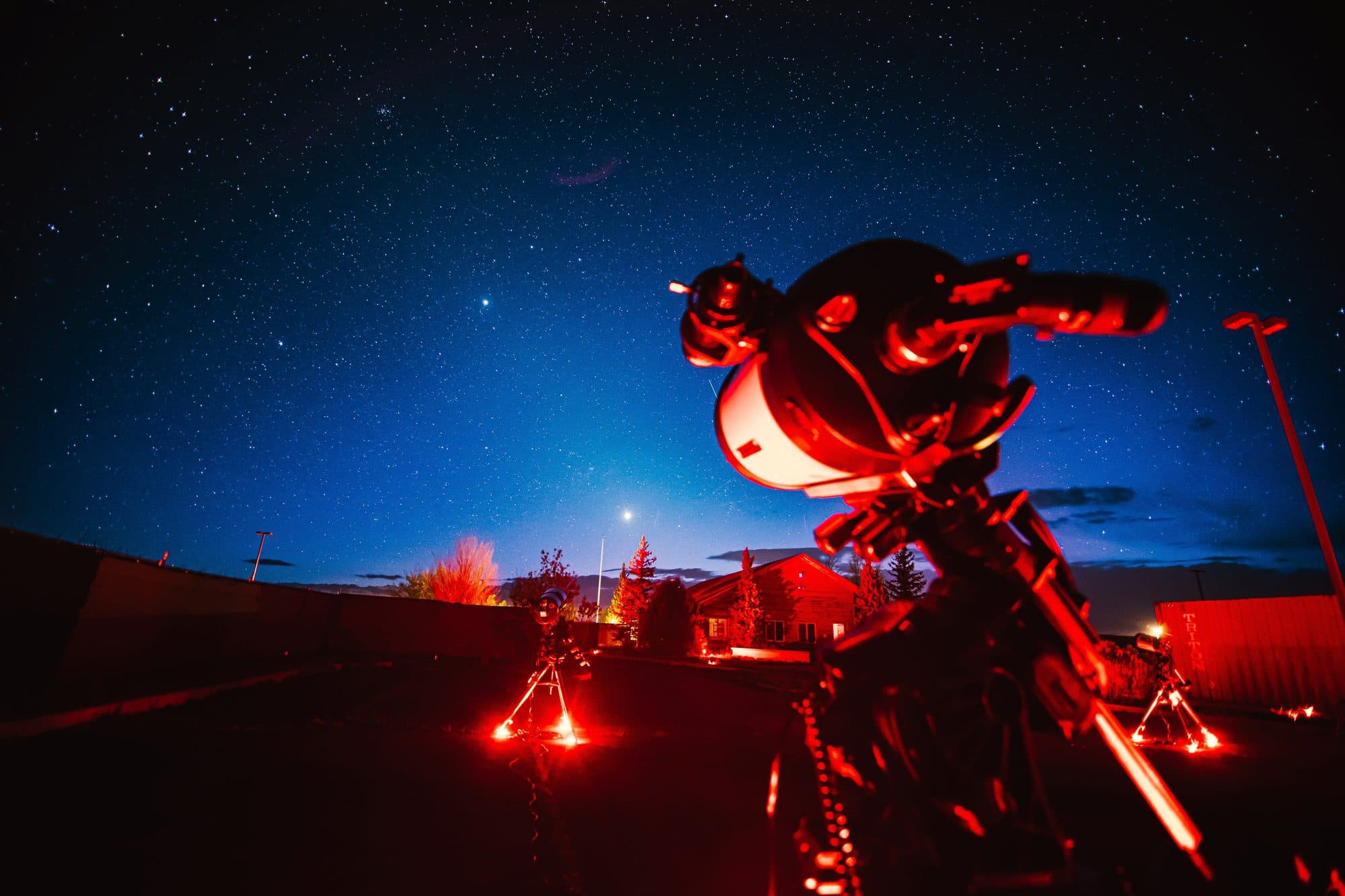 A telescope and mount lit red against the last blue of the horizon