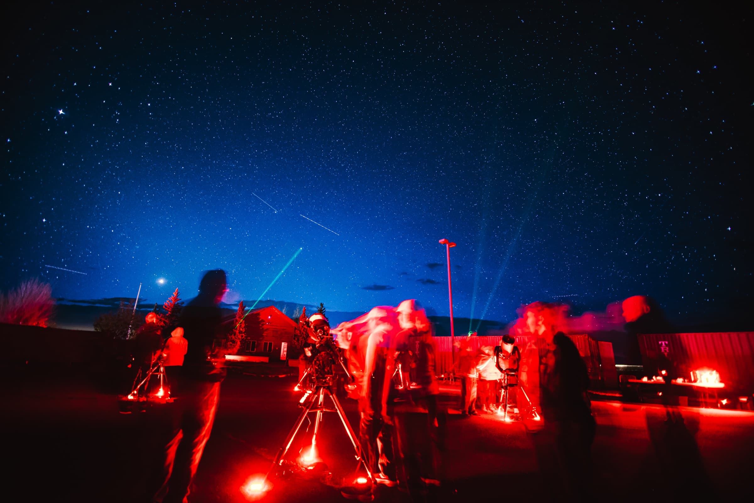 Guests moving between the telescopes at blue hour as a guide's green laser points into the sky