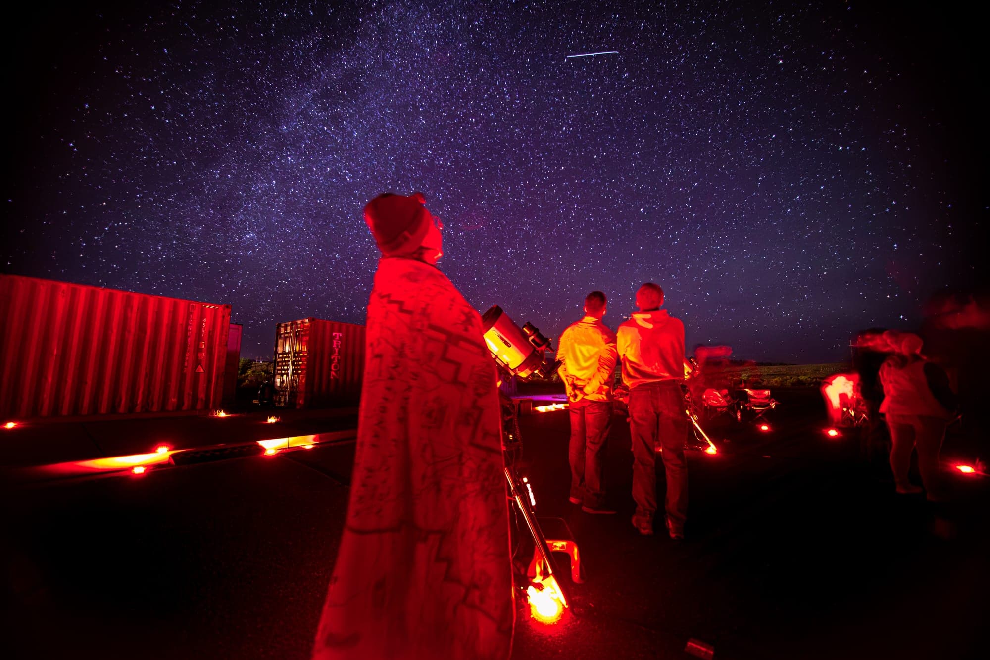 A guest wrapped in a blanket looking up at the Milky Way beside the telescopes