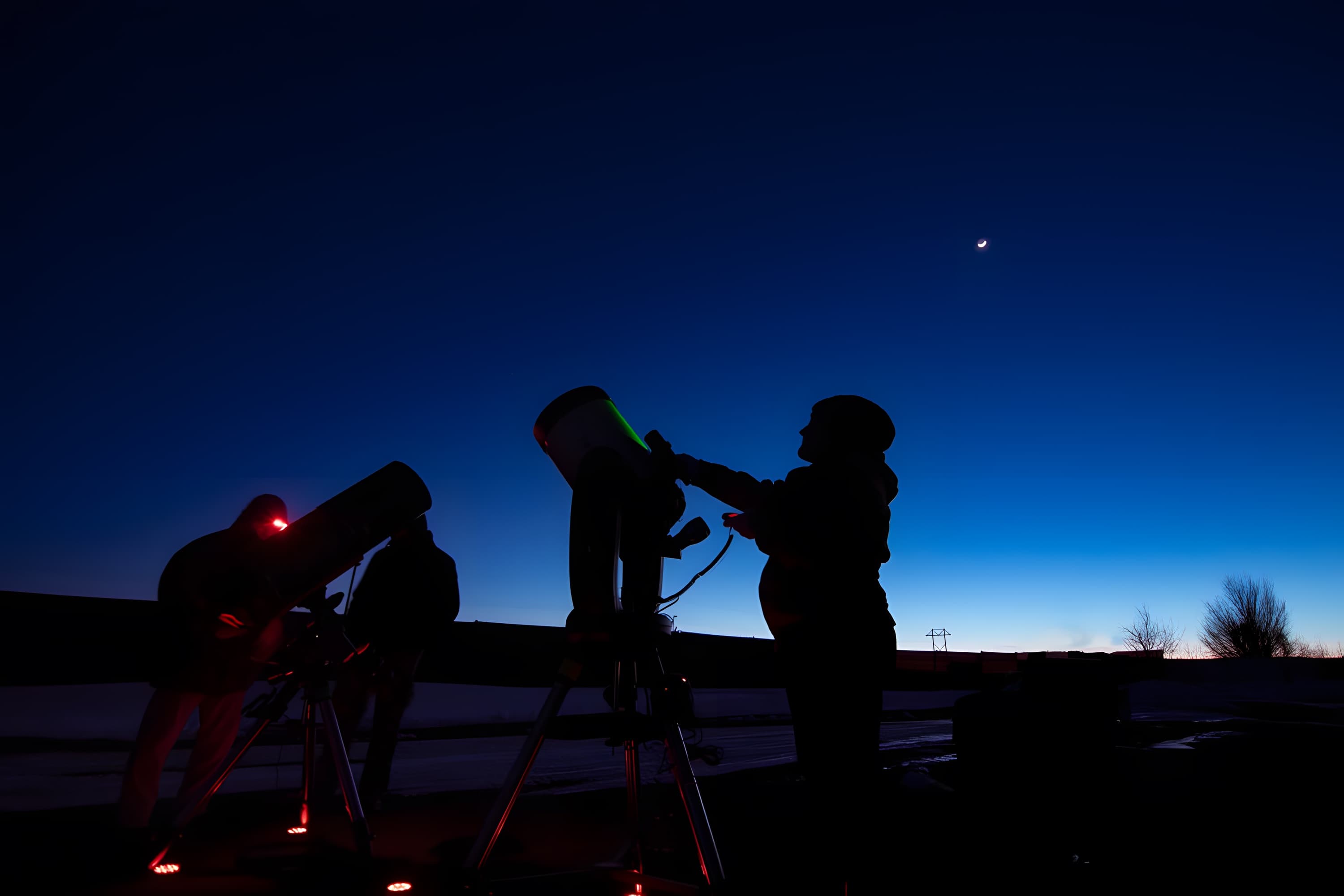 Three telescopes silhouetted against a twilight sky with a crescent moon
