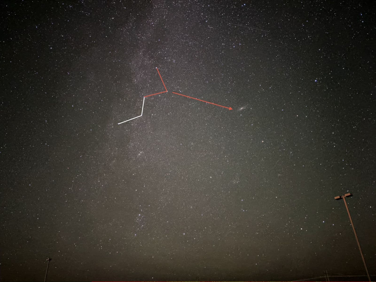 Night sky photograph with the W of Cassiopeia traced in red and an arrow pointing from its lowest star to the faint smudge of the Andromeda Galaxy